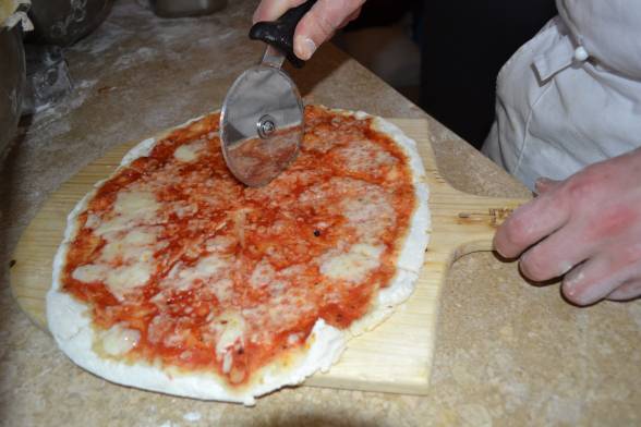 Готову піцу розрізати на частини, прикрасити свіжими листочками базиліка